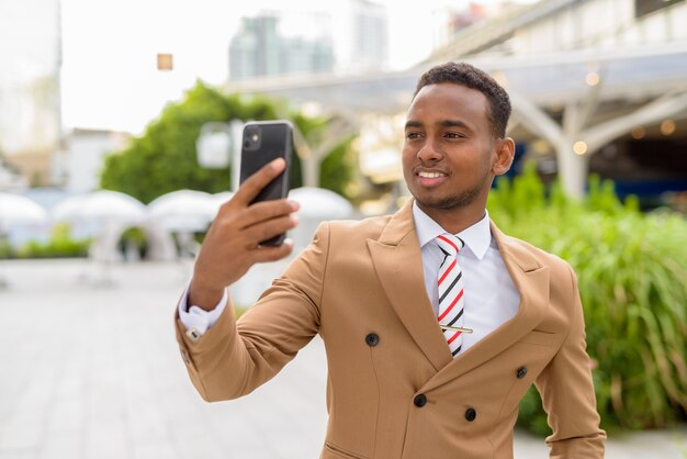 Heureux jeune homme d'affaires africain beau prenant selfie dans la ville