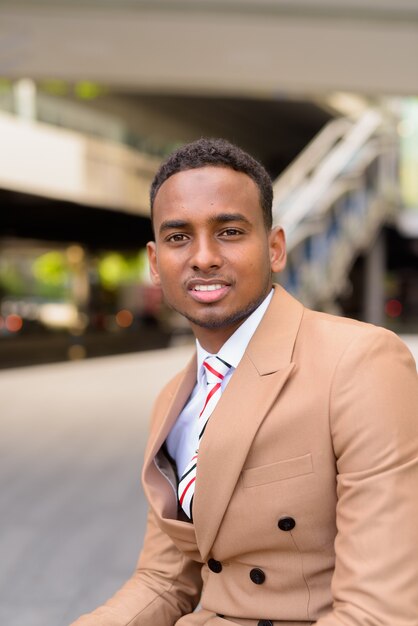 Heureux jeune homme d'affaires africain beau souriant dans la ville en plein air