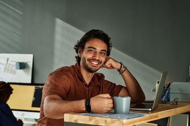 Heureux jeune homme d'affaires assis sur le lieu de travail au bureau