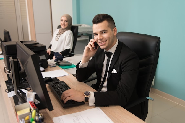 Heureux jeune homme d'affaires et femme musulmane travaillent dans un bureau moderne sur ordinateur