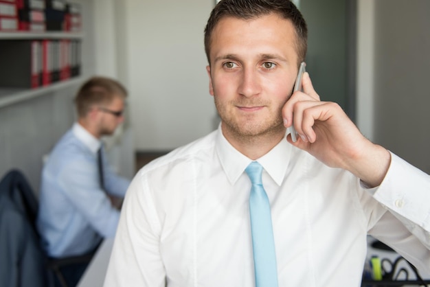 Heureux jeune homme d'affaires parlant au téléphone dans un bureau moderne derrière lui assis son collègue