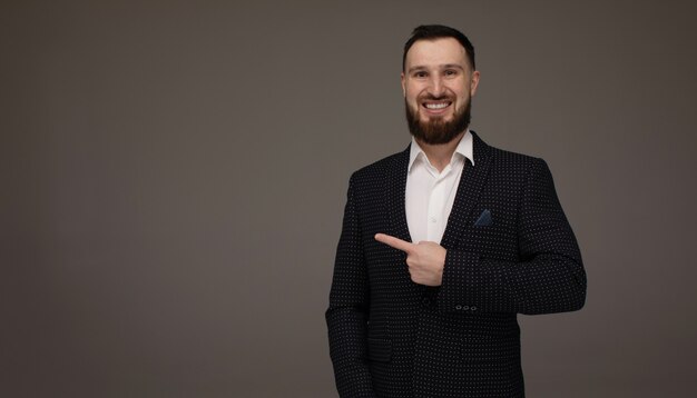 Heureux jeune homme d'affaires présentant isolé sur mur gris. Copyspace.