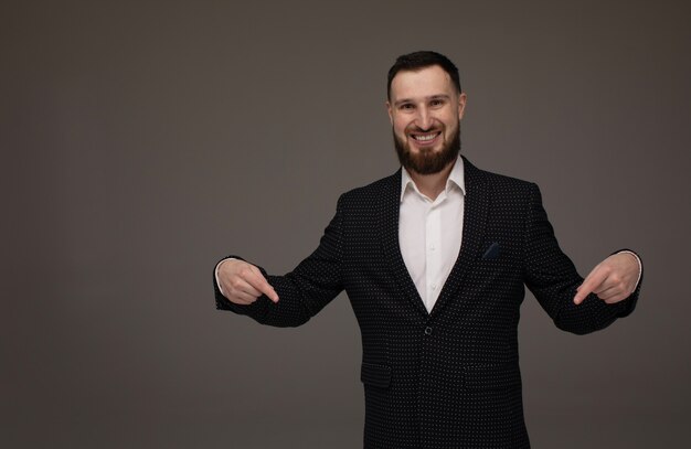 Heureux jeune homme d'affaires présentant isolé sur mur gris. Copyspace.