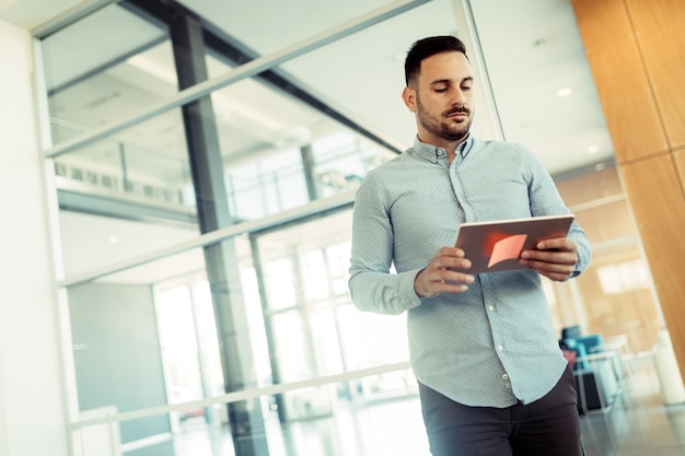 Heureux jeune homme d'affaires tenant une tablette dans un bureau moderne