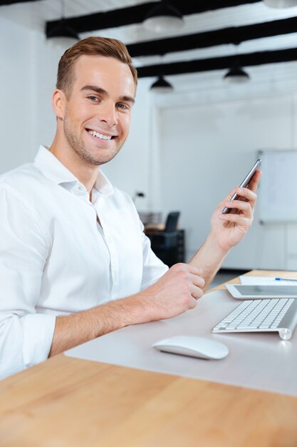 Heureux jeune homme d'affaires travaillant et utilisant un smartphone au bureau