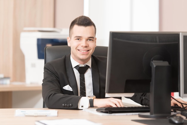 Heureux jeune homme d'affaires travaille dans un bureau moderne sur ordinateur