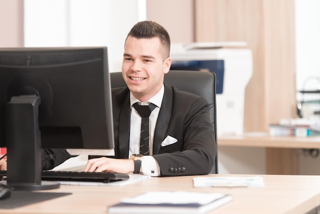 Heureux jeune homme d'affaires travaille dans un bureau moderne sur ordinateur