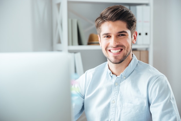 Heureux jeune homme d'affaires utilisant un ordinateur portable au bureau et regardant la caméra