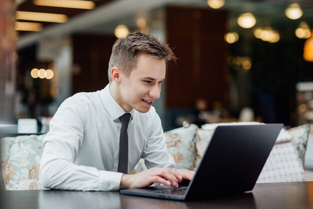 Heureux jeune homme d'affaires utilisant un ordinateur portable, vêtu d'une chemise blanche, dans un centre commercial