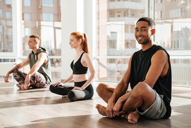 Heureux jeune homme africain assis et faire du yoga en groupe