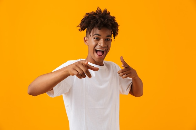 Heureux jeune homme africain posant isolé sur un espace jaune pointant.