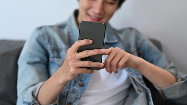 Heureux jeune homme asiatique envoyant un message texte surfant sur le web sur un téléphone intelligent à la maison
