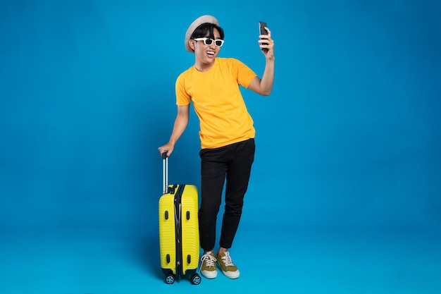 Heureux jeune homme asiatique heureux touriste avec des bagages sautant isolé sur fond de studio bleu