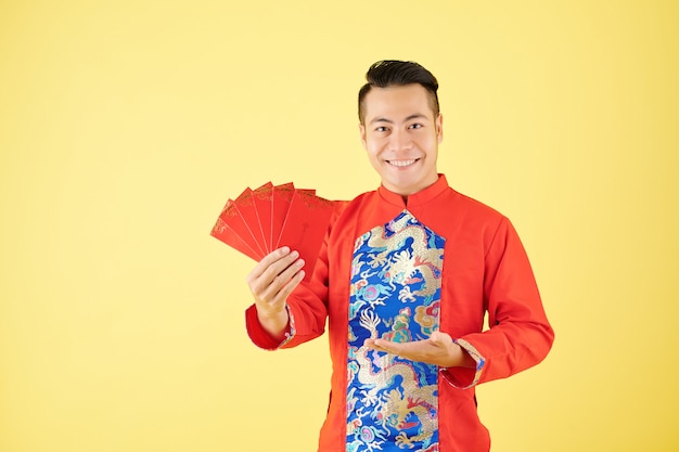 Heureux jeune homme asiatique montrant des enveloppes d'argent chanceuses qu'il a préparées pour la célébration du Nouvel An chinois