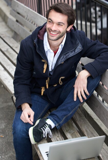 Heureux jeune homme assis sur un banc avec un ordinateur portable