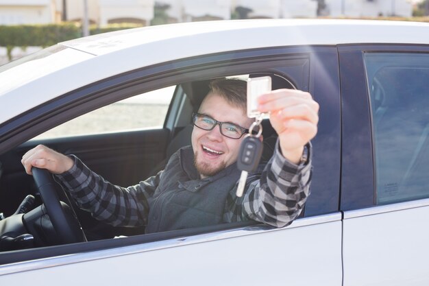 Heureux jeune homme assis dans la voiture tenant des clés de voiture