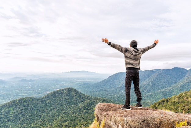 Heureux jeune homme au sommet de la montagne répandre la main et profiter de la vue sur la vallée vallée.