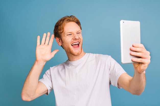 heureux jeune homme aux cheveux roux barbu en utilisant une tablette et debout