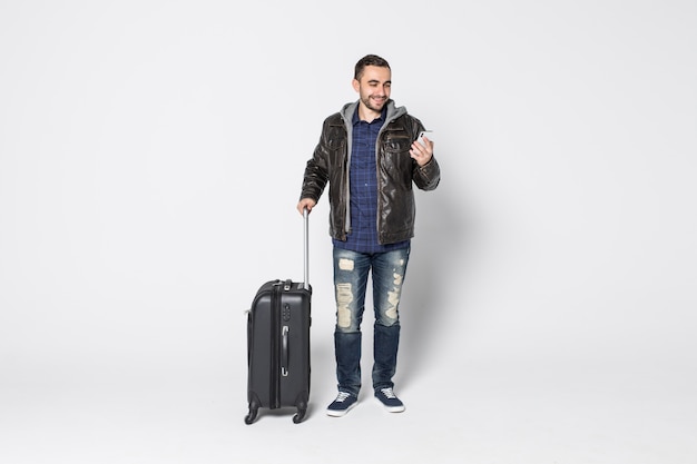 Heureux jeune homme avec des bagages utiliser smartphone isolé sur fond blanc