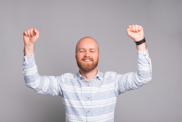 Heureux jeune homme avec barbe en casual célébrant la victoire sur fond gris