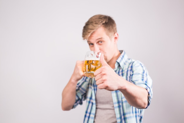 Heureux jeune homme buvant une chope de bière et montrant les pouces vers le haut