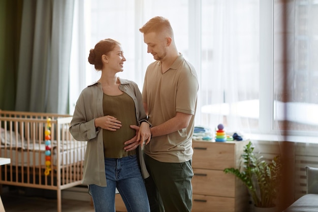 Heureux jeune homme caressant le ventre de sa femme enceinte alors qu'ils se tenaient dans la chambre d'enfant