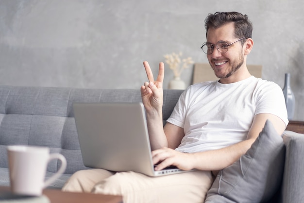 Heureux jeune homme chat vidéo sur ordinateur portable alors qu'il était assis sur le canapé à la maison