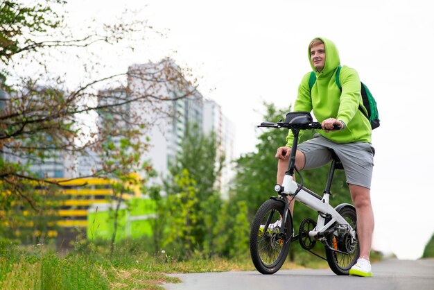 Heureux jeune homme chevauchant un vélo électrique dans un parc d'été, sports de style de vie actif