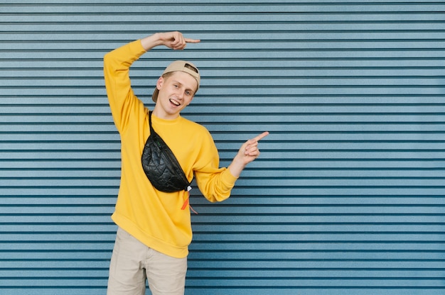 Heureux jeune homme dans un sweat-shirt jaune et une casquette montre ses mains à l'endroit vide