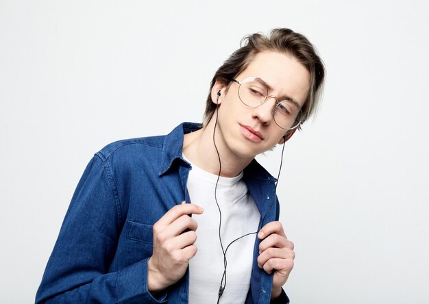 Heureux jeune homme élégant portant des vêtements décontractés et des lunettes ajustant ses écouteurs et souriant