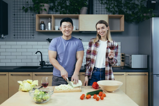 Heureux jeune homme et femme de famille cuisinant ensemble des légumes coupés asiatiques datent à la maison soirée romantique