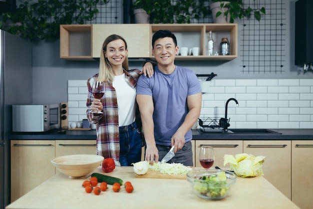 Heureux jeune homme et femme de famille cuisinant ensemble des légumes coupés asiatiques datent à la maison soirée romantique