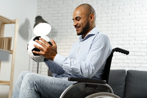 Heureux jeune homme handicapé en fauteuil roulant tenant un ballon de football et souriant