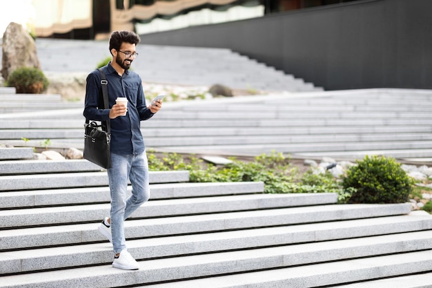 Heureux jeune homme indien tenant un smartphone marchant dans les escaliers