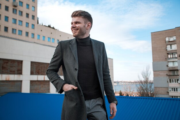 Heureux jeune homme à lunettes noires et un manteau gris