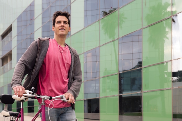 Heureux jeune homme marchant par la ville avec un vélo