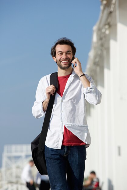 Heureux jeune homme marchant et parlant sur téléphone portable