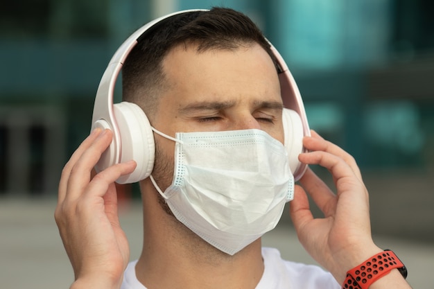 Heureux Jeune Homme En Masque Médical De Protection écouter De La Musique Avec Des écouteurs Bluetooth Sans Fil. Coronavirus Covid-19.