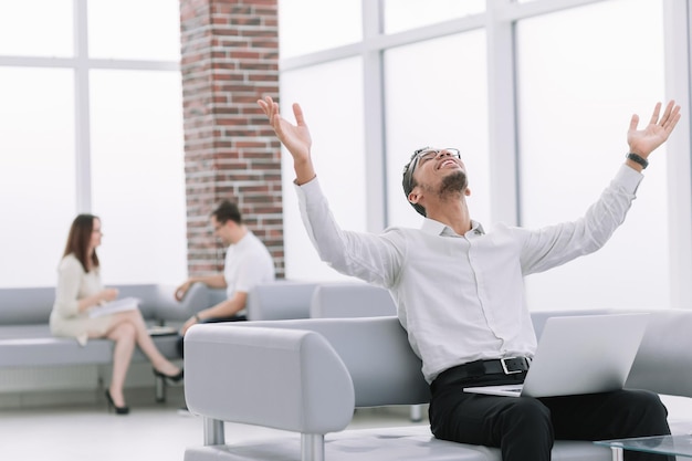 Heureux jeune homme avec un ordinateur portable assis sur un canapé de bureau