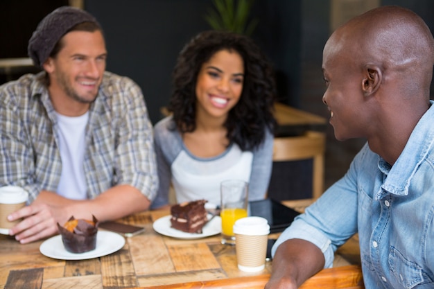 Heureux jeune homme parlant avec des amis à table dans un café