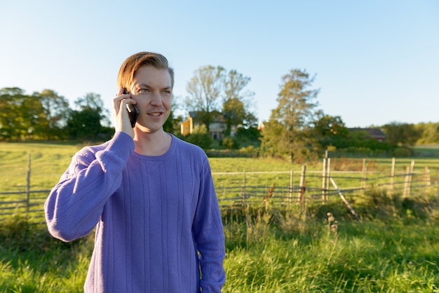 Heureux jeune homme parlant au téléphone mobile dans une plaine herbeuse paisible avec la nature