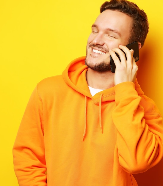 Heureux jeune homme parlant au téléphone portable sur fond jaune