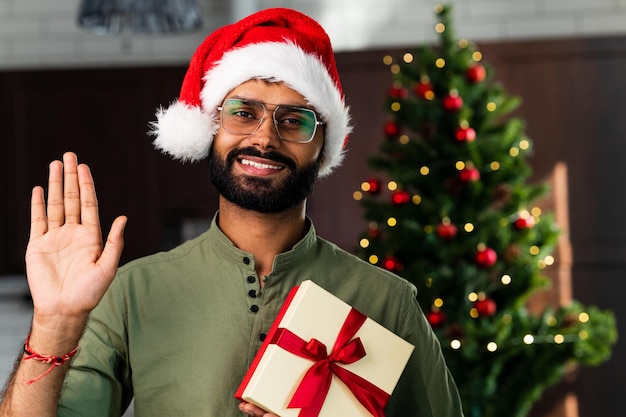 Heureux jeune homme portant un bonnet de Noel regardant la caméra célébrant la fête en ligne à distance du Nouvel An