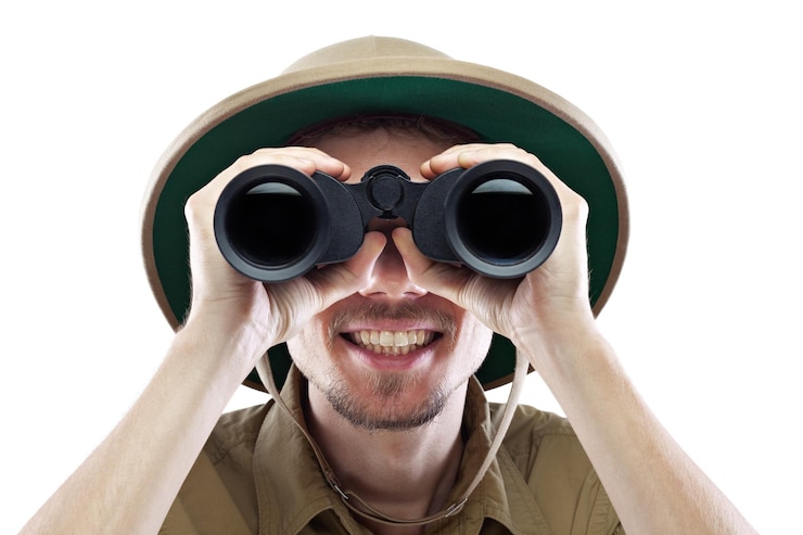 Photo heureux jeune homme portant une chemise safari et un casque colonial regardant à travers des jumelles