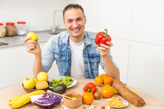 Heureux jeune homme préparant un dîner romantique à la recherche de recettes de légumes menu diététique, mari souriant cuisinant une salade de coupe de nourriture végétalienne saine à l'intérieur de la cuisine.