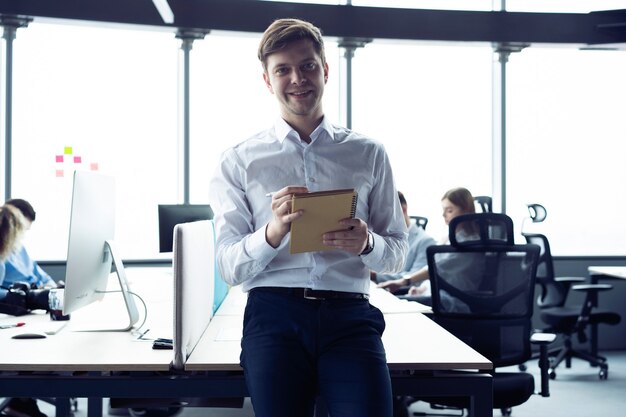 Heureux jeune homme souriant à la caméra avec une tablette à la main.