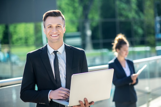 Heureux jeune homme souriant avec ordinateur portable à l'extérieur