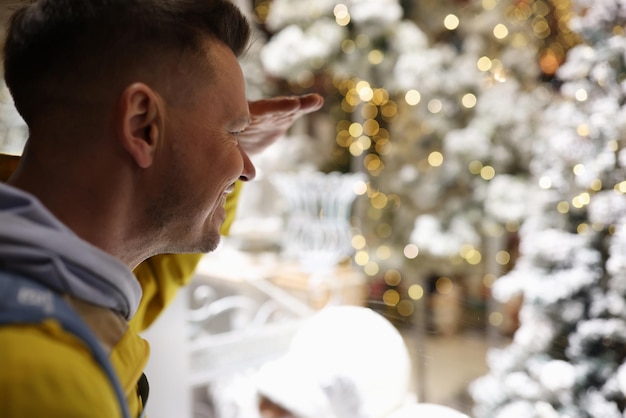 Heureux jeune homme souriant regardant la décoration de noël dans l'esprit de noël de la rue et