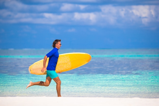 Heureux jeune homme surfant sur la plage avec une planche de surf