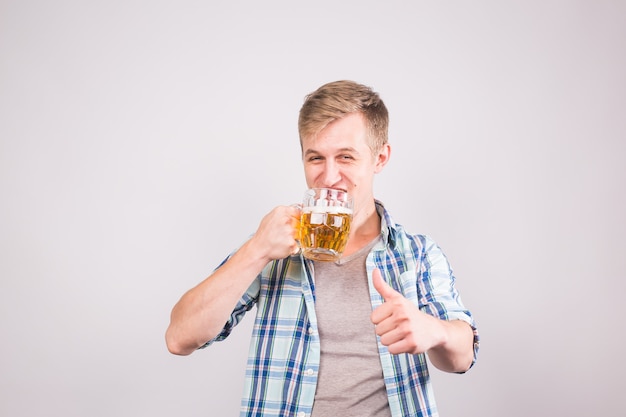 Heureux jeune homme tenant une chope de bière et montrant les pouces vers le haut.